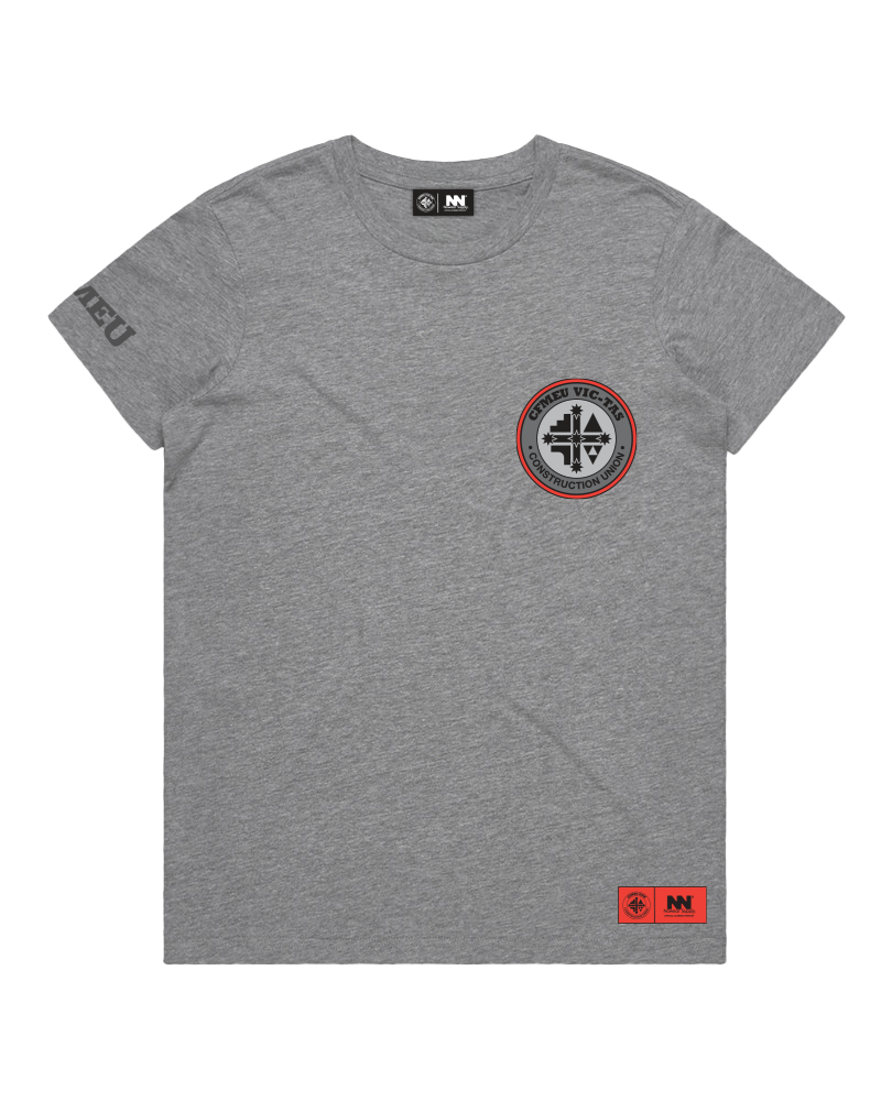 Gray crew-neck T-shirt with a left-chest circular patch (black cross, red ring) and an orange branding tag at the bottom-right hem; faint text on the left sleeve.