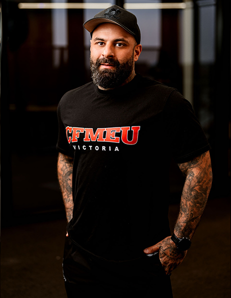 Portrait of a bearded man in a black CFMEU Victoria T-shirt and cap, standing with hands in pockets.