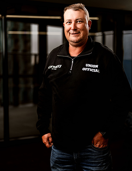 Smiling man in a black quarter-zip sweatshirt labeled Union Official, standing indoors with hands in pockets.